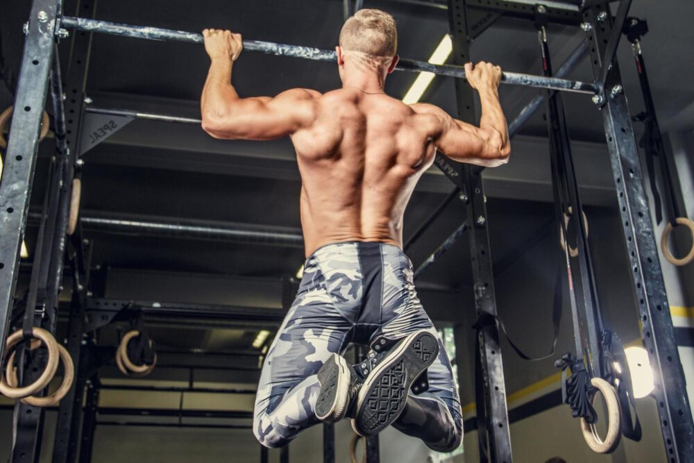 homme torse nu tirant barre horizontale dans salle sport